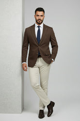 Man in brown and beige slim-fit two-piece suit with navy tie and brown shoes.